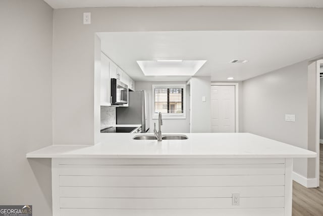 kitchen with sink, a skylight, light wood-type flooring, kitchen peninsula, and white cabinets