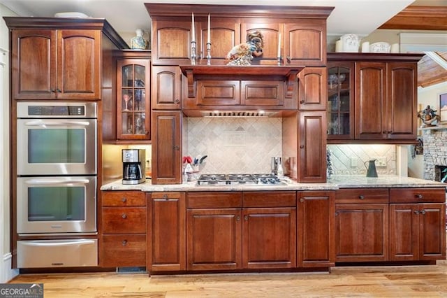 kitchen with appliances with stainless steel finishes, light hardwood / wood-style flooring, light stone counters, backsplash, and ornamental molding