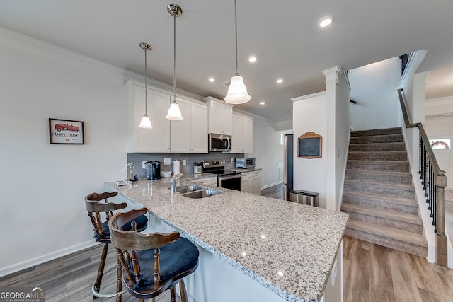 kitchen with pendant lighting, kitchen peninsula, sink, appliances with stainless steel finishes, and white cabinets