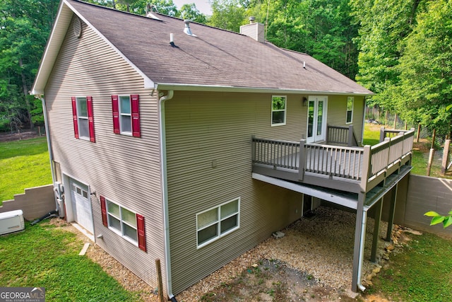 rear view of house with a shingled roof, a wooden deck, a chimney, a garage, and a yard