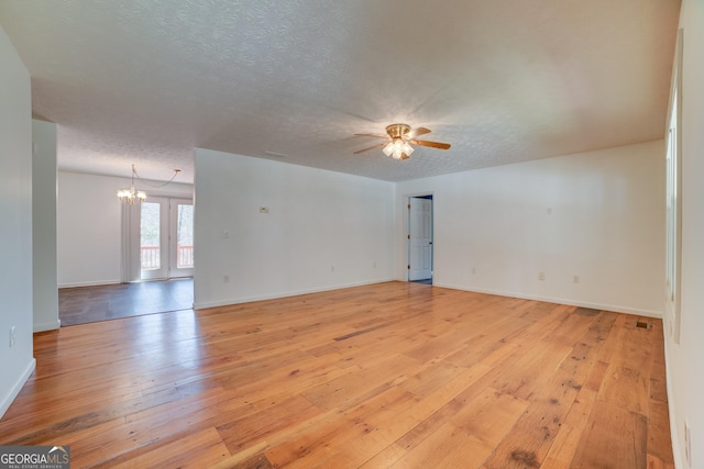 spare room with light wood finished floors, ceiling fan with notable chandelier, a textured ceiling, and baseboards