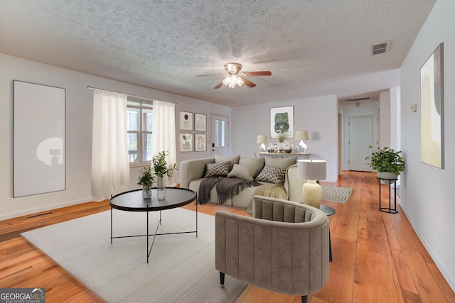 living area featuring light wood-style floors, visible vents, and a textured ceiling