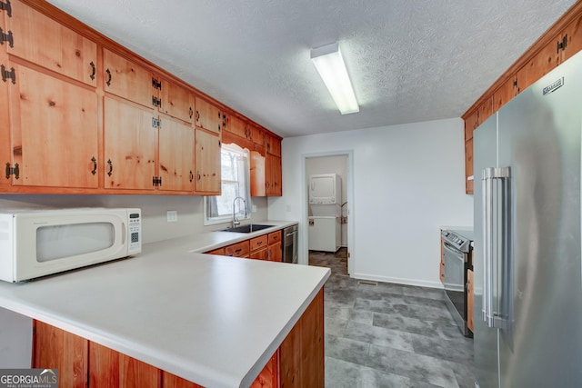 kitchen featuring stacked washer / dryer, light countertops, appliances with stainless steel finishes, a peninsula, and a sink