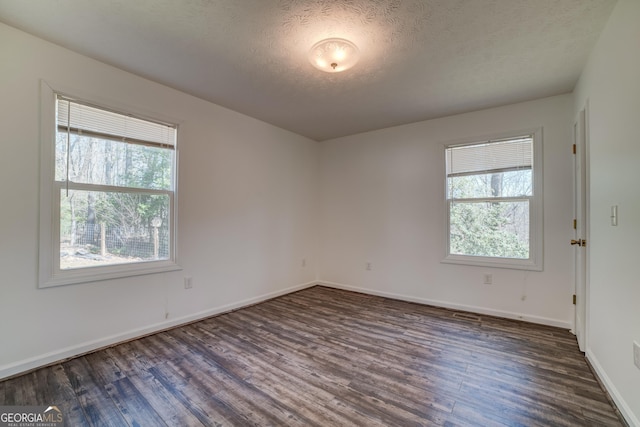 spare room featuring a healthy amount of sunlight, a textured ceiling, baseboards, and dark wood-style flooring