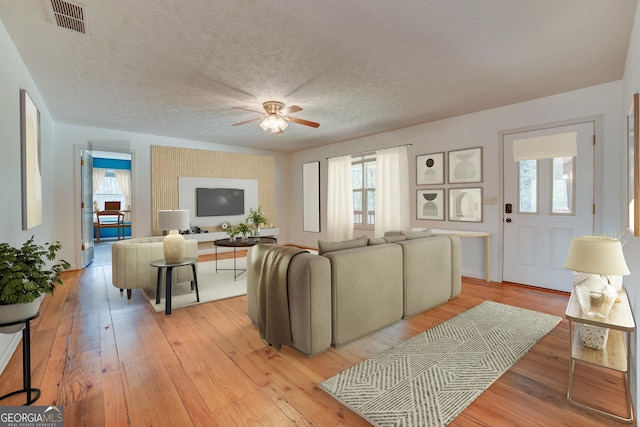 living room featuring a ceiling fan, visible vents, light wood finished floors, and a textured ceiling