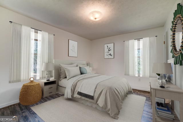 bedroom featuring baseboards, multiple windows, a textured ceiling, and wood finished floors