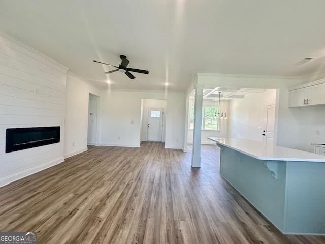 unfurnished living room with crown molding, dark hardwood / wood-style flooring, a large fireplace, and ceiling fan