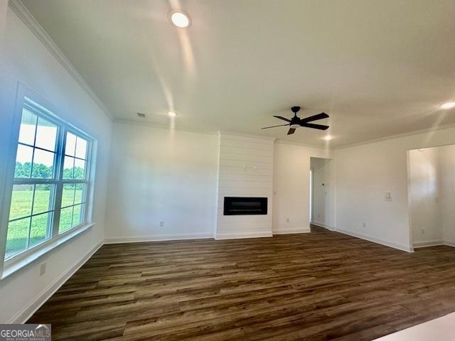 unfurnished living room with dark hardwood / wood-style flooring, crown molding, a large fireplace, and ceiling fan