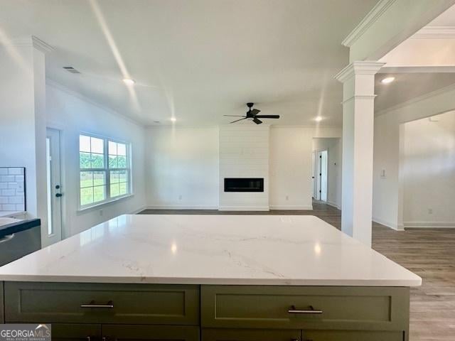 kitchen featuring ceiling fan, a fireplace, light stone countertops, and decorative columns