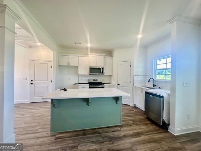 kitchen with sink, appliances with stainless steel finishes, white cabinetry, ornamental molding, and a kitchen island