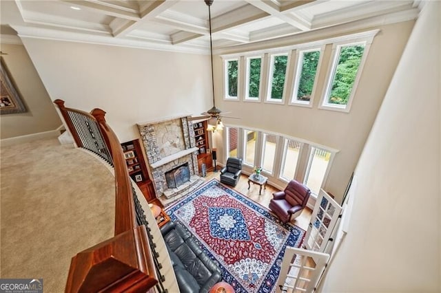 carpeted living room featuring ceiling fan, beamed ceiling, coffered ceiling, a fireplace, and a towering ceiling