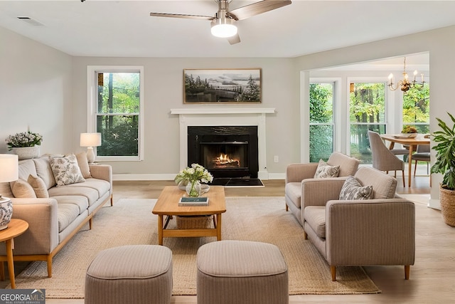 living area featuring light wood finished floors, a warm lit fireplace, visible vents, and baseboards