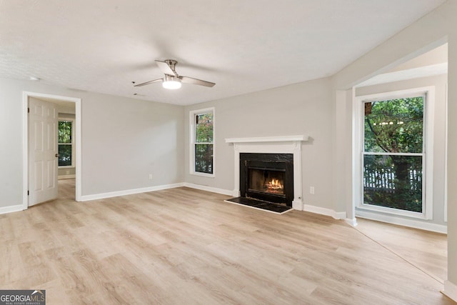 unfurnished living room featuring light wood-style floors, a fireplace, baseboards, and a ceiling fan