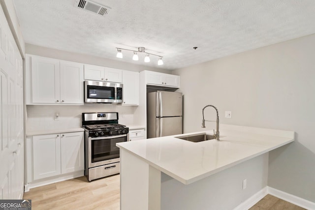 kitchen with a peninsula, white cabinetry, appliances with stainless steel finishes, and light countertops