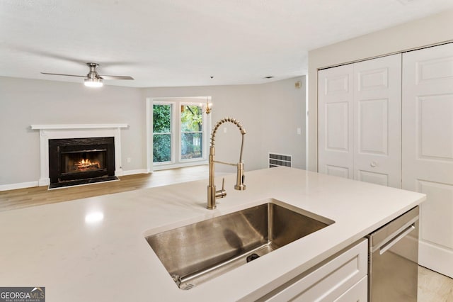 kitchen with light countertops, light wood-style flooring, stainless steel dishwasher, open floor plan, and a sink