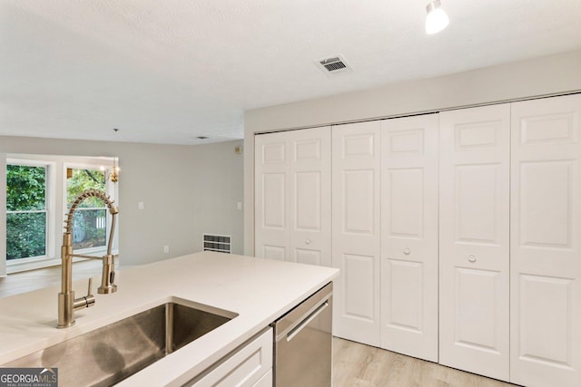 kitchen with visible vents, white cabinets, light countertops, stainless steel dishwasher, and a sink