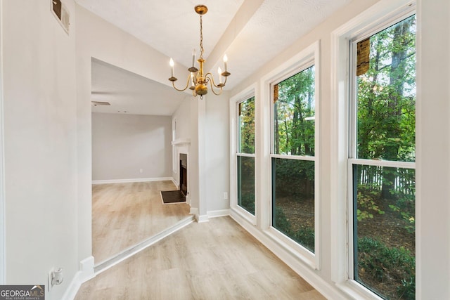 unfurnished dining area with a chandelier, a fireplace with flush hearth, wood finished floors, visible vents, and baseboards