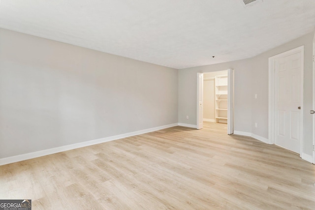 unfurnished bedroom with light wood-type flooring, baseboards, a walk in closet, and a closet