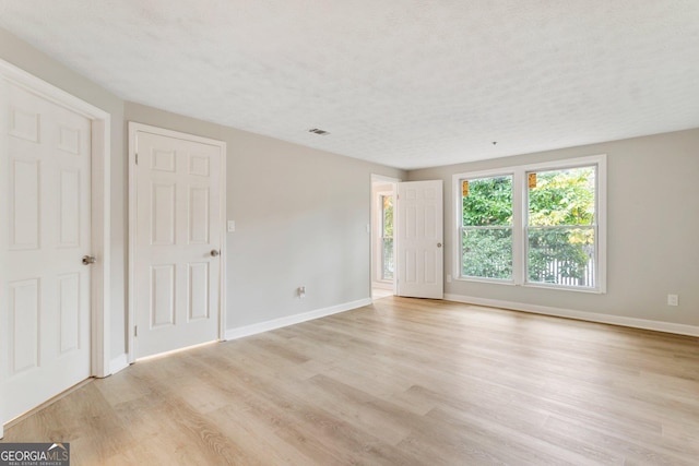 unfurnished room featuring light wood-style floors, visible vents, a textured ceiling, and baseboards