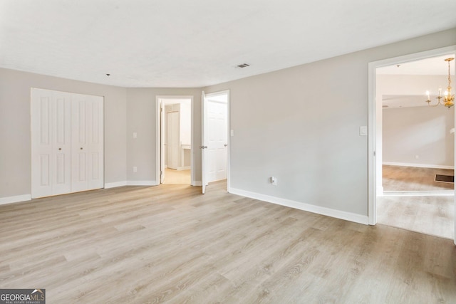 unfurnished bedroom featuring a notable chandelier, a closet, baseboards, and light wood-style floors