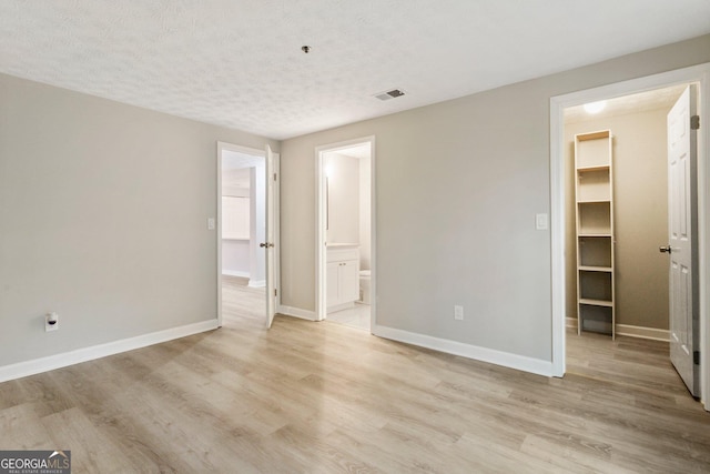 unfurnished bedroom featuring light wood-style flooring, a walk in closet, visible vents, and baseboards