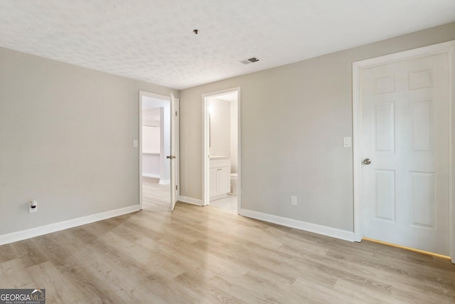 unfurnished bedroom with a textured ceiling, light wood-style flooring, visible vents, and baseboards