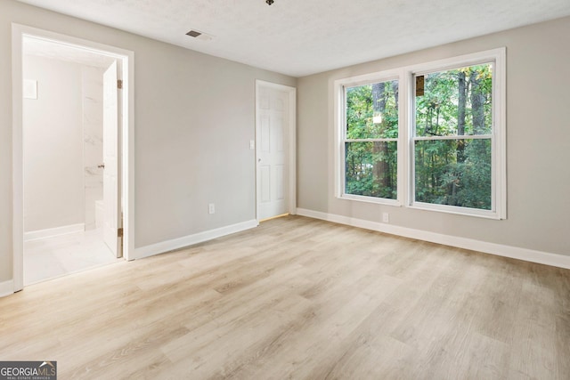 unfurnished bedroom with baseboards, visible vents, a textured ceiling, and light wood finished floors