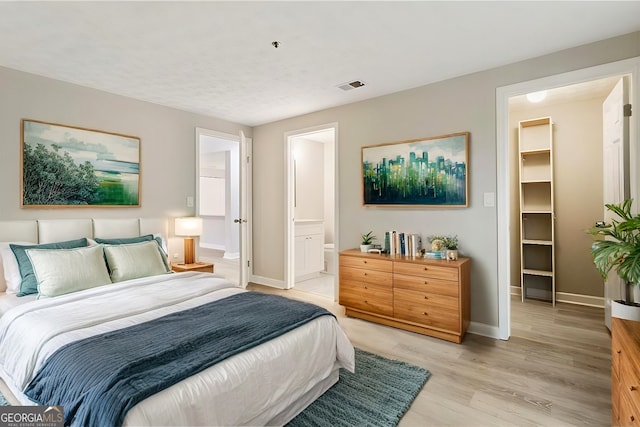 bedroom with visible vents, a spacious closet, ensuite bathroom, light wood-type flooring, and baseboards