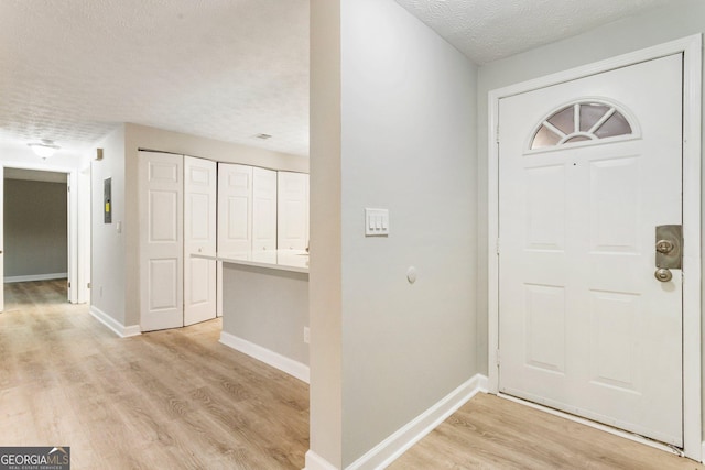 foyer featuring baseboards, a textured ceiling, and light wood finished floors