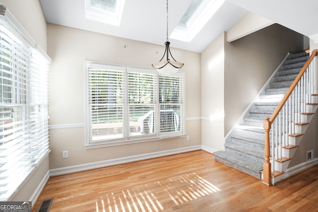 unfurnished dining area featuring vaulted ceiling with skylight and hardwood / wood-style floors