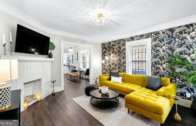 living room featuring a fireplace, an inviting chandelier, ornamental molding, a textured ceiling, and dark hardwood / wood-style flooring