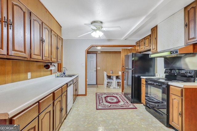 kitchen featuring ceiling fan, sink, black appliances, and wood walls