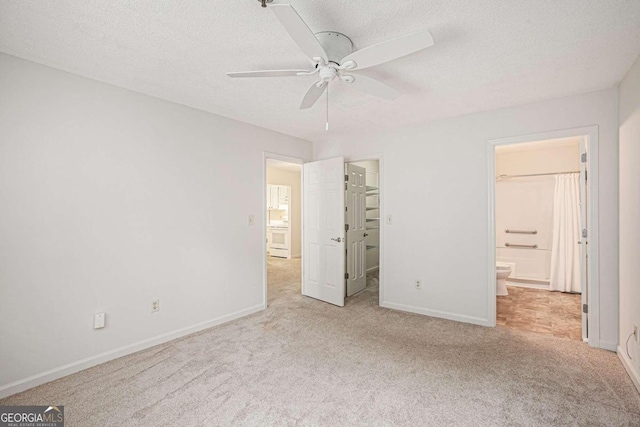 unfurnished bedroom with ceiling fan, ensuite bathroom, a textured ceiling, light carpet, and a spacious closet