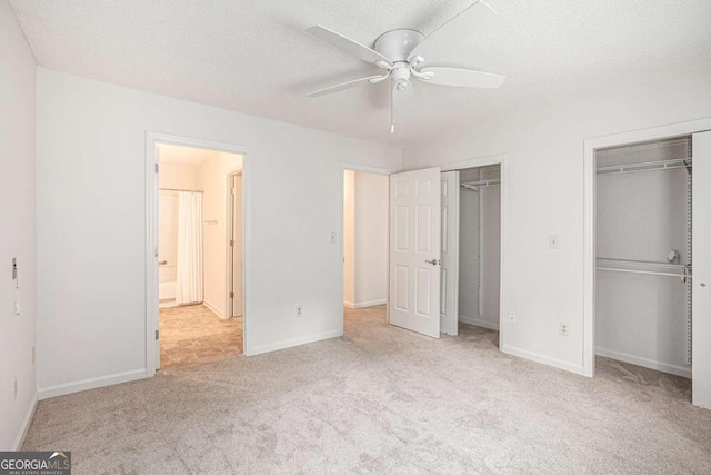 unfurnished bedroom with ceiling fan, a textured ceiling, light colored carpet, and multiple closets