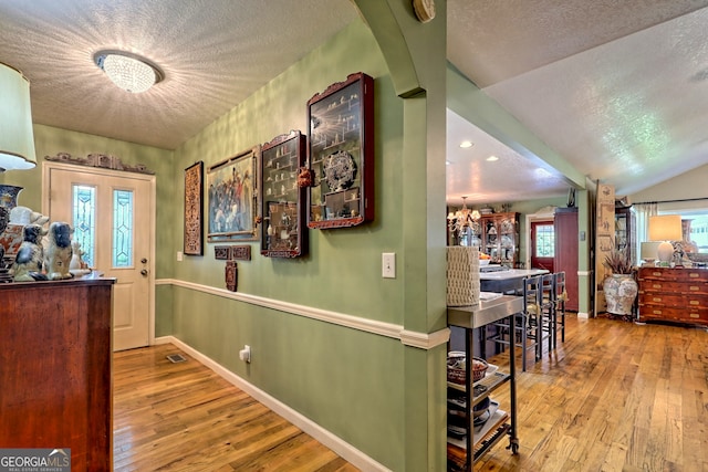 hall featuring a textured ceiling, hardwood / wood-style flooring, lofted ceiling, and a notable chandelier