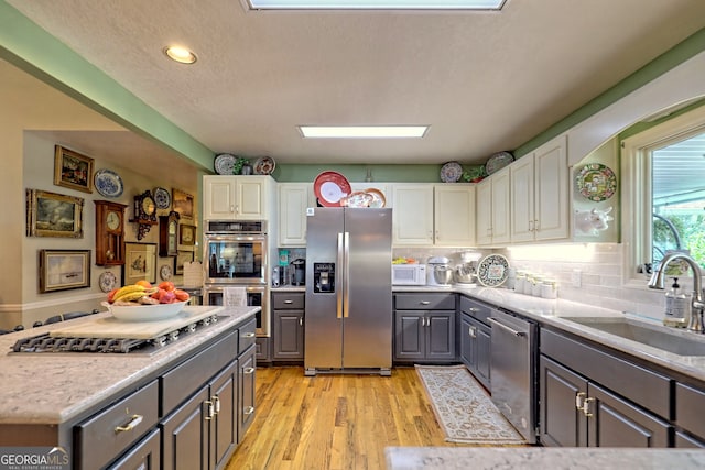 kitchen with light wood-type flooring, gray cabinets, stainless steel appliances, decorative backsplash, and sink