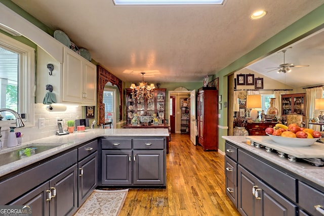 kitchen with light hardwood / wood-style flooring, vaulted ceiling, ceiling fan with notable chandelier, decorative light fixtures, and sink