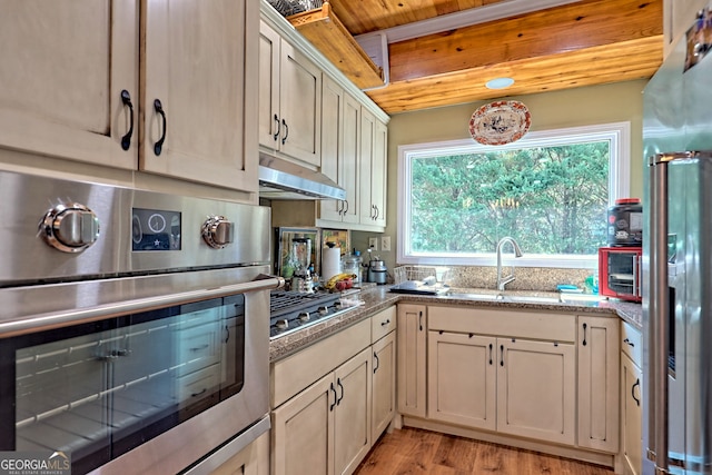 kitchen featuring appliances with stainless steel finishes, light hardwood / wood-style flooring, wood ceiling, sink, and light stone countertops