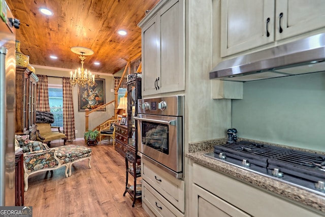 kitchen featuring appliances with stainless steel finishes, an inviting chandelier, hanging light fixtures, light wood-type flooring, and light stone countertops