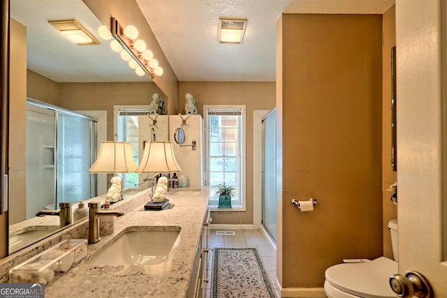 bathroom with toilet, a shower with door, tile patterned flooring, and dual bowl vanity