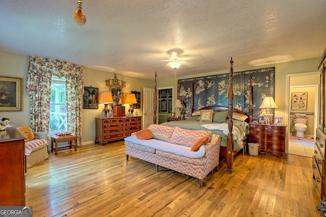 bedroom with light hardwood / wood-style floors, a textured ceiling, ceiling fan, and connected bathroom