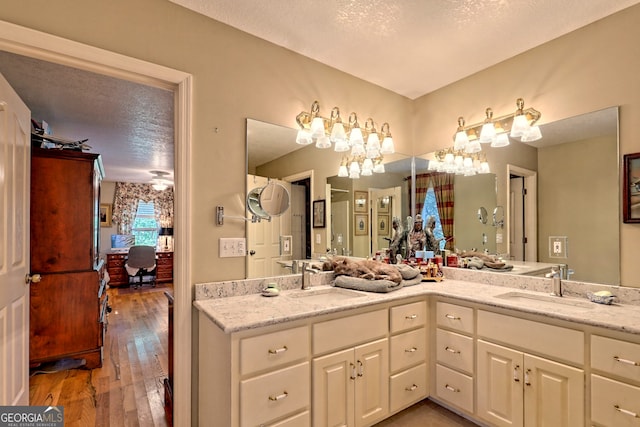 bathroom featuring a textured ceiling, wood-type flooring, and dual bowl vanity