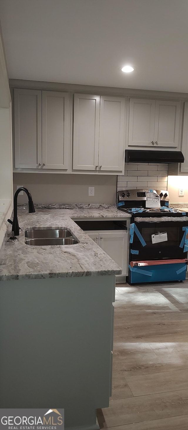 kitchen with light stone counters, sink, black electric range, and light wood-type flooring