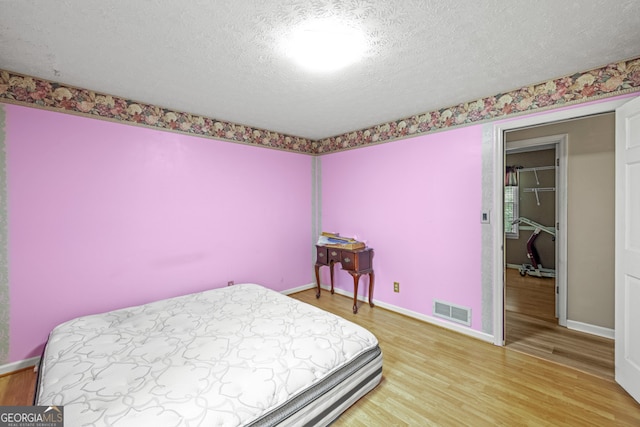 bedroom with hardwood / wood-style flooring, a closet, a textured ceiling, and a walk in closet