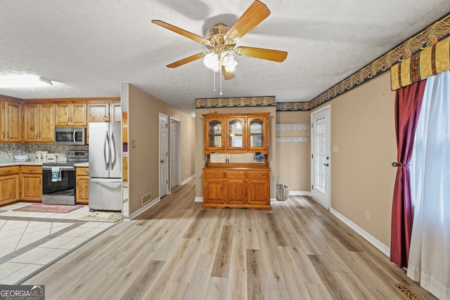 kitchen featuring ceiling fan, tasteful backsplash, a textured ceiling, light hardwood / wood-style flooring, and appliances with stainless steel finishes