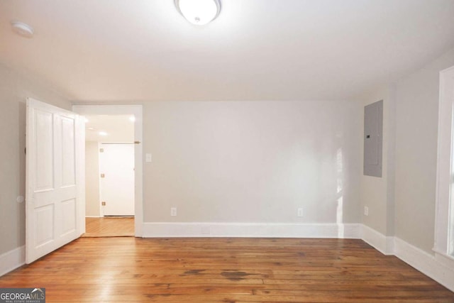 empty room with hardwood / wood-style floors, electric panel, and baseboards