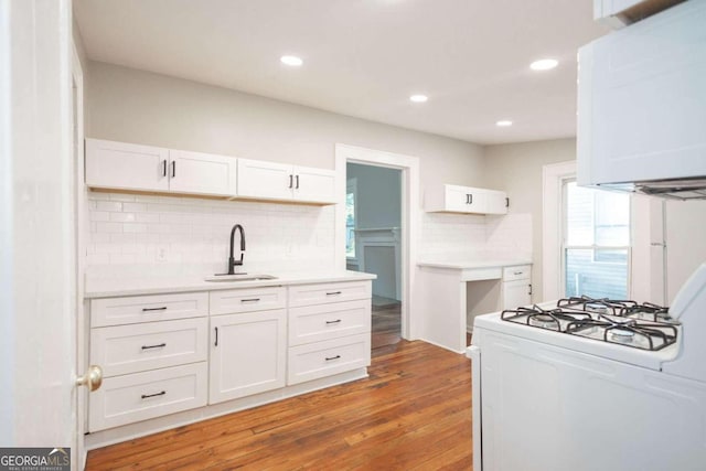 kitchen with white cabinets, wood-type flooring, white range with gas cooktop, tasteful backsplash, and sink