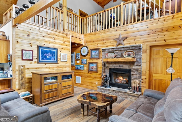 living room with wooden walls, a fireplace, light wood-type flooring, and a towering ceiling