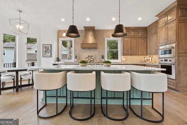 kitchen with a healthy amount of sunlight, a large island with sink, hanging light fixtures, and custom range hood