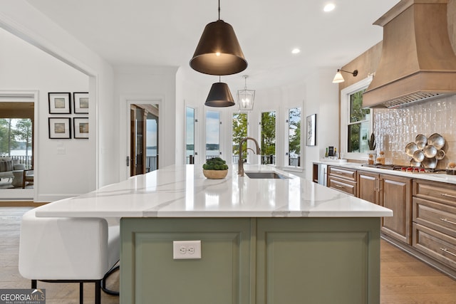 kitchen with an island with sink, light stone counters, and custom range hood